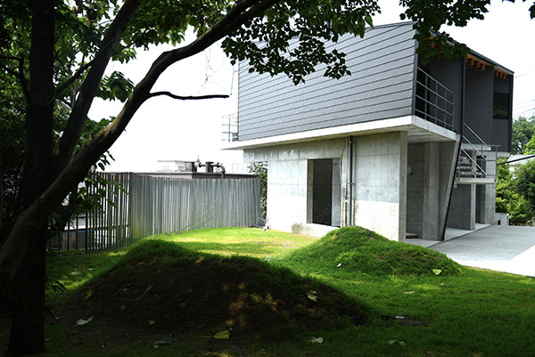 private villa tenの裏庭に広がる芝生と彫刻的な築山、アルミフェンスの調和